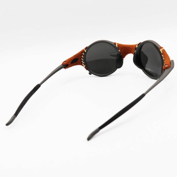 عکس از عینک آفتابی پلاریزه اوکلی با فریم گرد، چرمی، رنگ نوک مدادی و لنز آینه‌ای و نقره‌ای به همراه پک مدل 2541