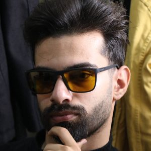 عکس از عینک شب OGA MOREL با فریم مشکی مات، مستطیلی شکل، دسته فنری و لنز زرد رنگ مدل 78013 بر روی صورت محمدحسین ابراهیم زاده