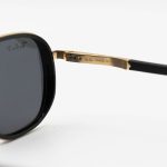 عکس از عینک آفتابی Ray-Ban با فریم مشکی و طلایی، شکل چند ضلعی، دسته فنری و لنز دودی تیره و پلاریزه مدل P9004