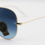 عکس از عینک آفتابی Ray-Ban با فریم خلبانی، رنگ طلایی، لنز از جنس سنگ، آبی تیره و هایلایت مدل RB3026 HQ