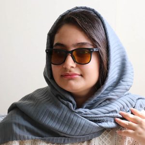 عکس از عینک دید در شب اوگا مورل با فریم مشکی مات، مربعی شکل، دسته فنری و لنز زرد رنگ مدل 78099 بر روی صورت فاطمه ابراهیم زاده