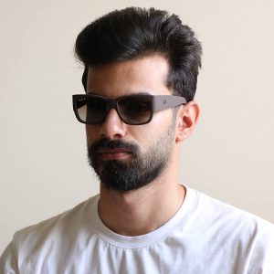 عکس از عینک آفتابی Ray-Ban با فریم قهوه ای مات، شکل مستطیلی، دسته پهن و لنز پلاریزه و قهوه‌ای هایلایت مدل RB2187 بر روی صورت محمدحسین ابراهیم زاده